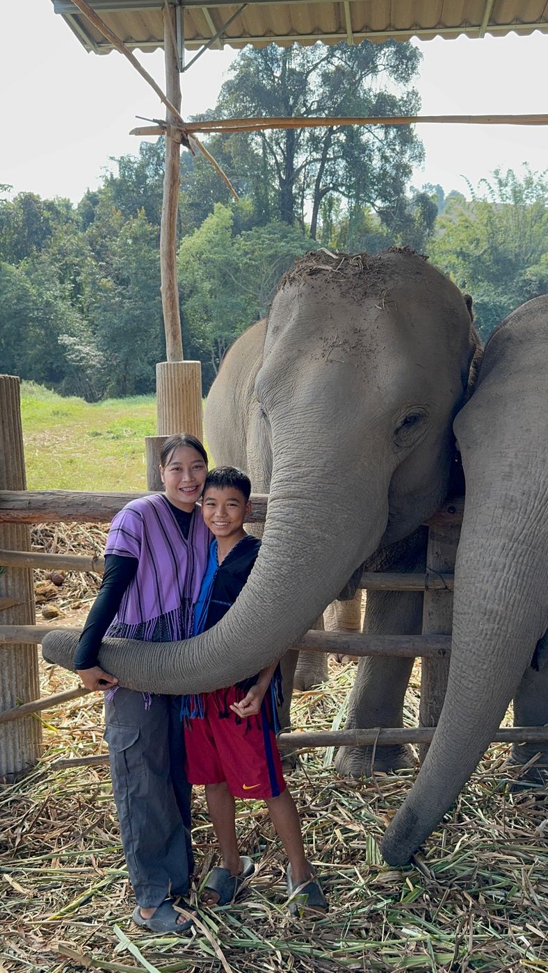 A woman and boy smiling beside an elephant with its trunk curled gently in front of them