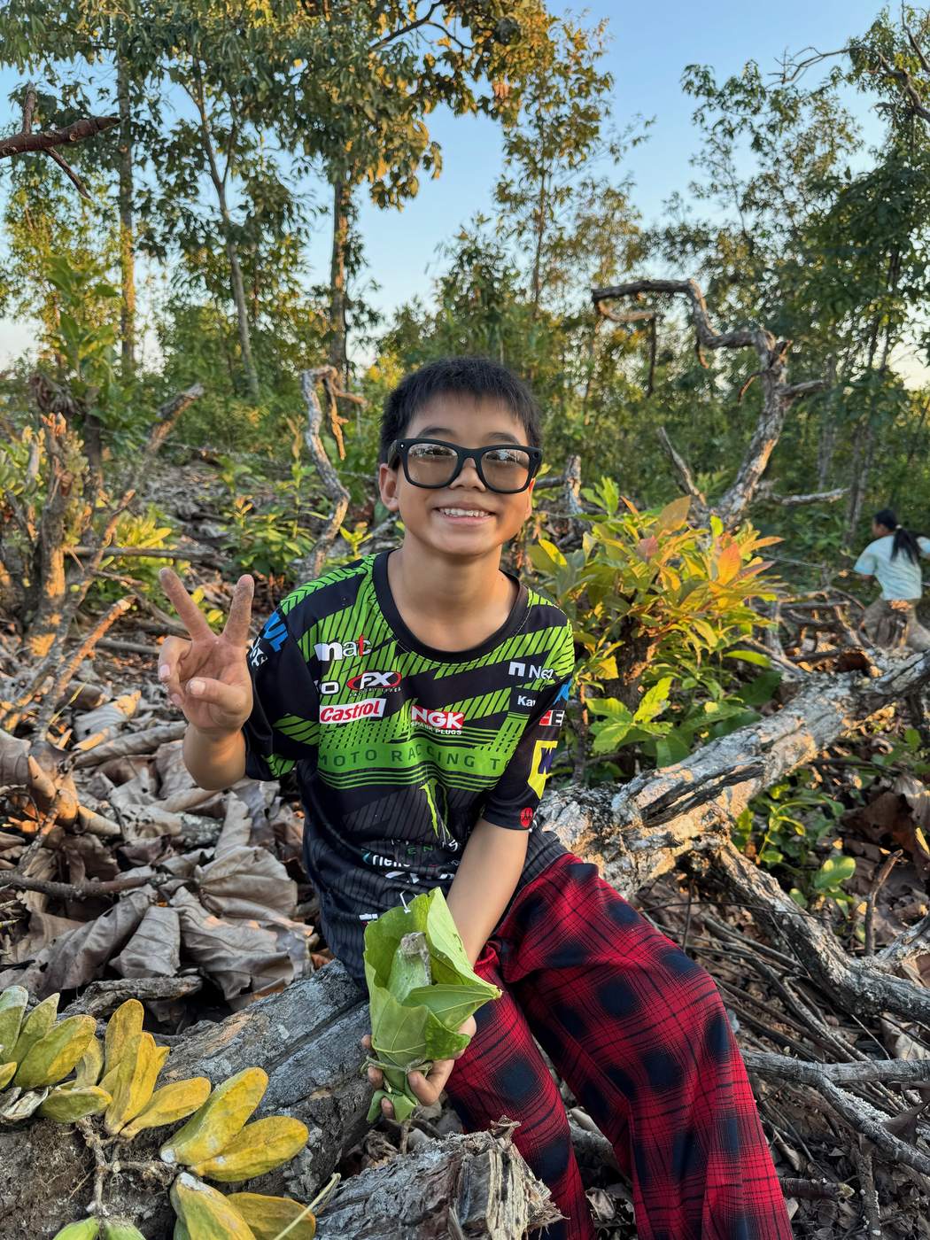 A smiling village boy holding a leaf-wrapped snack in warm forest light