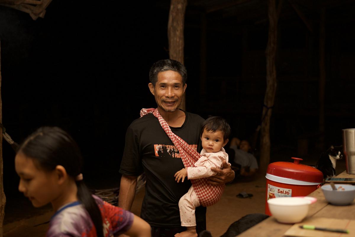 A villager holding a baby in a cloth sling at the evening gathering