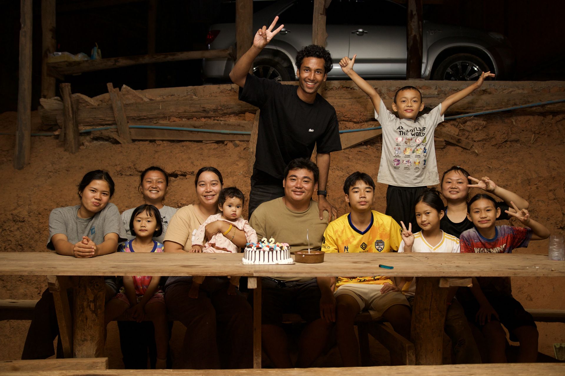 Villagers and guests gathered around a birthday cake on a long wooden table