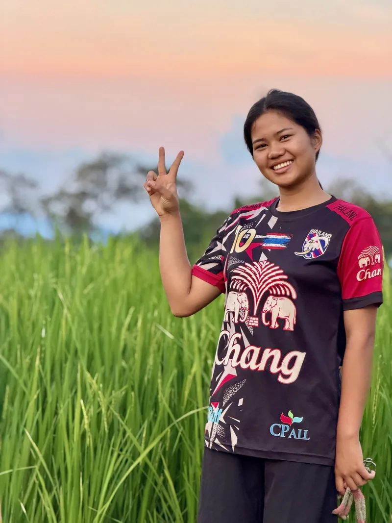 A smiling woman giving a peace sign beside the rice fields